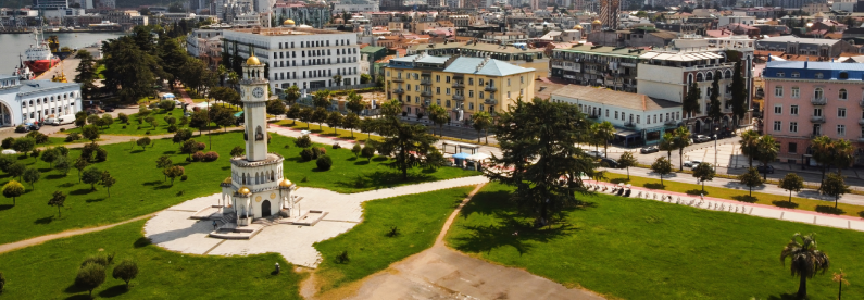 Aerial view of green park with tall clock tower and surrounding buildings, showing diverse architecture and serene vibe.